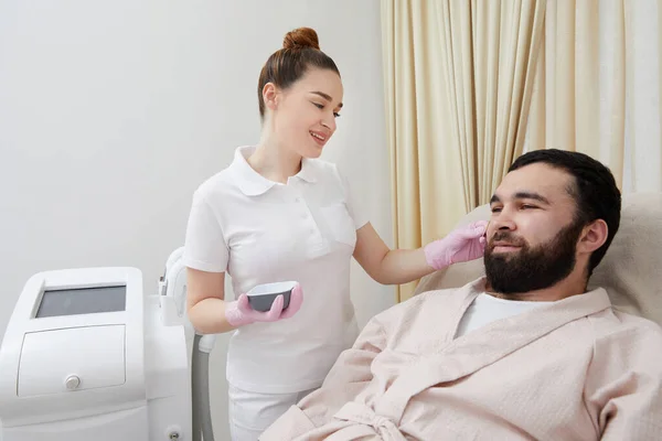 stock image Bearded man getting laser facial treatment by professional cosmetologist in a beauty clinic. Healthy man lifestyle concept