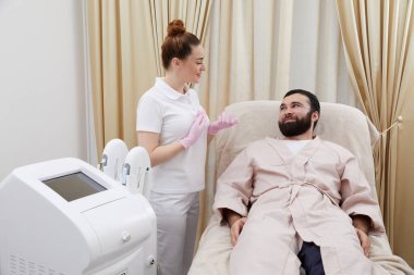 Güzellik uzmanı kozmetoloji dolabında genç bir adamla konuşuyor.