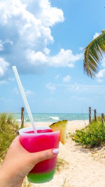 Bir bardakta kokteyl ve pipetle el ele tutuşmak ve Amerika 'daki Miami Beach, Florida' da okyanusa giden kum yolu.