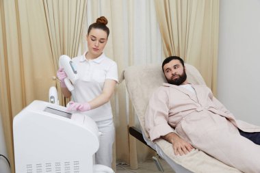 Modern bir kozmetoloji kliniğinde bir erkeğin yüzüne lazer tüyü tedavisi uygulanıyor.