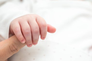 Uyuyan yeni doğmuş bir bebeğin annesinin parmağına sevgiyle tutunduğu huzurlu bir an.