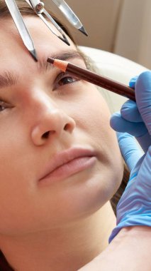 Kaşların şeklini değiştiriyorum. Cetvelle kaşları ölçen stilist. Güzellik salonunda mikro pigmentasyon işi. Kaşları yarı kalıcı makyajla boyanmış bir kadın..