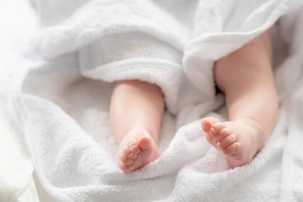 The delicate feet and legs of an infant child subtly peeking out from the pure whiteness of a soft towel after bathing