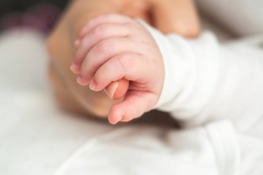 Rüya gören yeni doğmuş bir bebeğin yakın çekimi, annesinin elini sıkıca tutuyor, saf sevgi ve güven iletiyor.