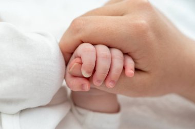 Yakın plan yeni doğmuş bir bebeği annelerinin başparmağına nazikçe tutunarak, doğuştan gelen bir bağ ve güven göstererek yakalar.