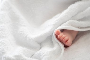 Yumuşak bir havlunun beyaz kucaklamasından zarif bir şekilde dışarı bakan bir bebeğin minik ayağını gösteren sevimli bir görüntü.