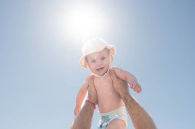 Bir babanın bebeğini güneşli gökyüzüne kaldırıp sevgiyi ve oyunculuğu sembolize ettiği iç açıcı bir sahne. Baba sevgisi kavramı ve mutlu anlar.