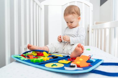 Bir yaşında bebek, Montessori ile oynuyor. Kitapla meşgul, beşikte oturuyor. Eğitim kitapları ve sessiz kitap konsepti. Montessori meşgul tahtası
