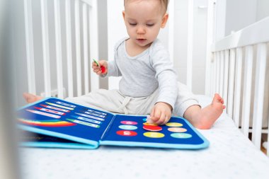 Bir yaşında bebek, Montessori ile oynuyor. Kitapla meşgul, beşikte oturuyor. Eğitim kitapları ve sessiz kitap konsepti. Montessori meşgul tahtası