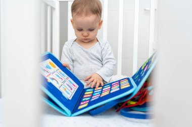 Bir yaşındaki bebek Montessori ile oynuyor. Kitapla meşgul, beşikte oturuyor.