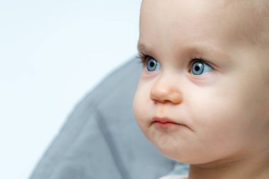 Mavi gözlü bir bebek yüksek bir sandalyede oturuyor, tatlı bir gülümseme, pembe yanaklar ve uzun kirpiklerle kameraya bakıyor.