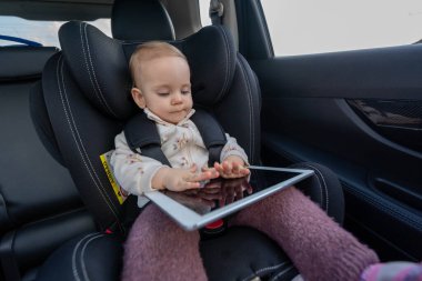 Sevimli küçük kız anaokuluna giderken araba koltuğunda tablet kullanıyor.