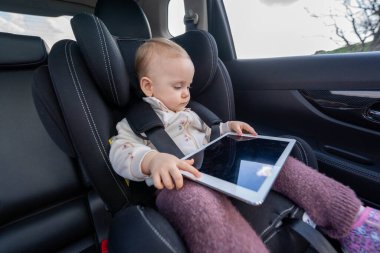 Sevimli küçük kız anaokuluna giderken araba koltuğunda tablet kullanıyor.