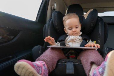 Küçük kız, uzun yolculukta çocuk oto koltuğunda dijital tablet kullanıyor. Araba koltuklarındaki çocuklar için güvenli ve eğlenceli seyahat kavramı