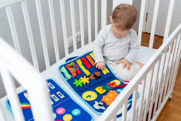 stock image One year old baby playing with montessori busy book sitting in crib