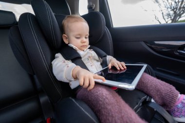 Sevimli küçük kız anaokuluna giderken araba koltuğunda tablet kullanıyor.