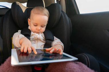 Uzun yolculukta çocuk koltuğunda dijital tabletli küçük bir kız. Yolculuklar sırasında çocuklar için rahat ve ilgi çekici seyahat kavramı