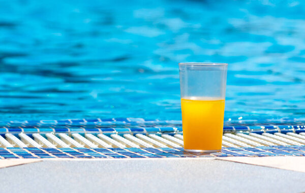 Стакан свежего прохладного апельсинового сока рядом с бассейном, концепция летнего тропического отдыха.