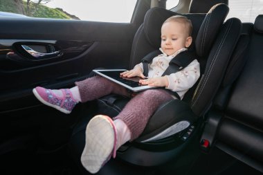 Bebek bebek koltuğunda otururken dijital tablet kullanıyor. Yolculuktaki çocukların teknoloji kullanımı kavramı, onları meşgul tutmak ve eğlendirmek.