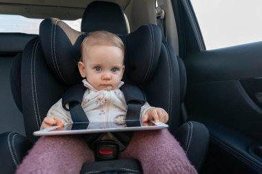 Sevimli küçük kız anaokuluna giderken araba koltuğunda tablet kullanıyor.