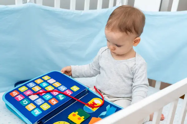 stock image One year old baby playing with montessori busy book sitting in crib