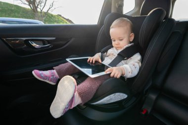 Küçük kız uzun yolculukta çocuk koltuğunda tablet kullanıyor. Dijital ilişki ve seyahat rahatlığı kavramı, teknolojinin çocukları nasıl eğlendirdiğine odaklanmak