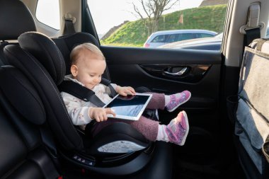 Sevimli küçük kız anaokuluna giderken araba koltuğunda tablet kullanıyor.