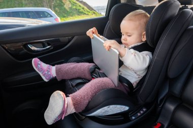 Sevimli küçük kız anaokuluna giderken araba koltuğunda tablet kullanıyor.
