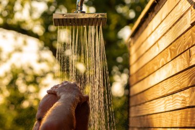 Gün batımında doğa tarafından çevrelenmiş, ferahlatıcı bir duşun tadını çıkaran bir adam. Sakin bir ortamda rahatlama ve doğal banyo kavramı