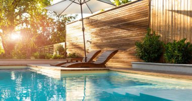 Günbatımında ahşap güneşlik ve palmiye ağaçları sergilenen modern villa havuzu lüks ve şık bir açık hava alanı yaratıyor. Lüks bir ortamda rahatlık ve rahatlık kavramı