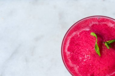 Nane süslemesi ve samanla dolu, mermer zemin üzerine kurulmuş canlı kırmızı donmuş bir içeceğin yukarıdan aşağıya bakışı. Serin serinleme, yaz rahatlığı ve tropikal keyif kavramı