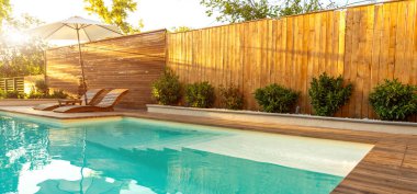 Güneş pansiyonları ve yeşil çitlerle çevrili ahşap bir çitin bulunduğu şık bir havuz kenarı, özel ve lüks bir açık hava inzivası yaratıyor. Huzur, mahremiyet ve lüks rahatlama kavramı