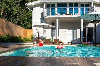 Küçük çocuklu ebeveynler sıcak güneşin altında, villa havuzunda rahatlatıcı bir gün geçiriyorlar. Tatil boyunca aile birliği, mutluluk ve boş zaman kavramı
