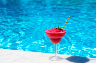 Havuzun yanındaki bardakta donmuş kırmızı kokteyl ve güneşli bir arka plan. Tropikal ferahlama ve yaz tatilinde serinleme kavramı