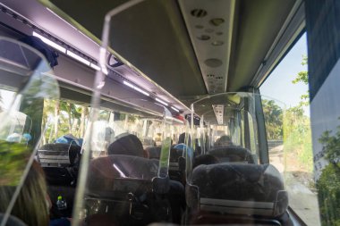 Günışığıyla aydınlatılan saydam COVID koruyucu bariyerlerin arkasında oturan yolcuların oturduğu modern bir otobüsün içi. Salgın sırasında toplu taşımada güvenlik ve konfor kavramı