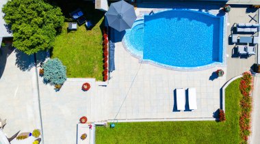 Temiz mavi suyu, çevresindeki verandası ve yeşil çimenliği olan lüks bir yüzme havuzunun havadan görünüşü. Açık hava yaz rahatlaması ve modern bahçe tasarımı kavramı