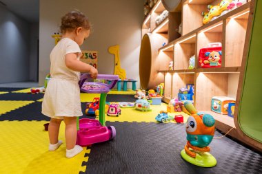 Bebek renkli bir oyun odasında oyuncak arabası itiyor. Oyuncak oyuncaklarla dolu. Erken öğrenim kavramı ve oyun yoluyla yaratıcılık