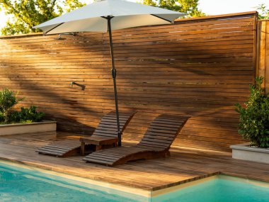 Parlak ahşap güvertesi, rahat şezlongları ve gölgesi için büyük bir şemsiyesi olan güneşli havuz kenarı.