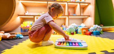 Bebecik, parlak bir oyun odasında renkli bir piyanoyla oynuyor.