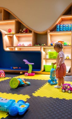 Küçük çocuk oyuncaklarla, raflarla ve yaratıcı tasarımlarla dolu kapalı alanda eğleniyor.