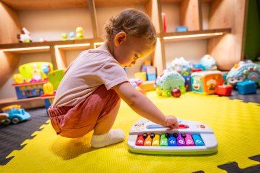 Canlı bir oyun alanında oyuncak bir piyanoyla müziği keşfeden küçük bir çocuk.