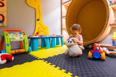Modern oyun alanındaki oyuncaklar ve eğitimsel oyunlarla çevrili yumuşak oyun hasırlarında oturan küçük çocuk