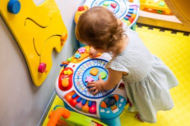 Bebecik, parlak bir oyun odasında renkli bir aktivite masasını keşfediyor, şekilleri ve sesleri öğreniyor. Erken öğrenimi teşvik etme ve motor becerileri geliştirme kavramı