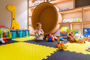 Pofuduk oyuncaklarla ve oyun alanındaki etkileşimli oyunlarla meşgul olan bebek.