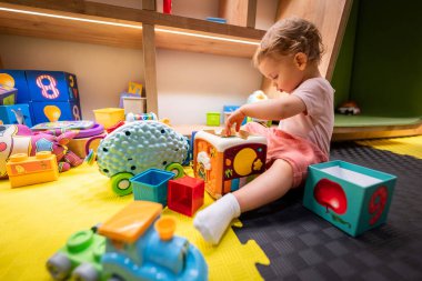 Çocuk neşeli bir oyun alanında yapı taşları ve etkileşimli oyuncaklarla meşgul.