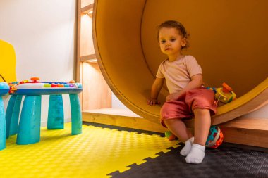 Canlı bir oyun odasında, etkileşimli oyuncaklar, aktivite tabloları ve erken öğrenim ve keşif için renkli tasarımlarla oynayan gülümseyen bebek.