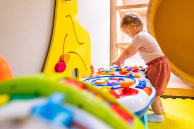 Çocuk, oyun alanında ışıklar, sesler ve şekiller içeren etkileşimli oyuncak masasıyla oynuyor.