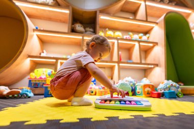 Parlak bir oyun odasında müzik oyuncağıyla oynarken motor becerilerini geliştiren bir çocuk.