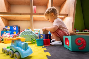 Child discovering colorful blocks and playful toys in a bright and inviting play space clipart