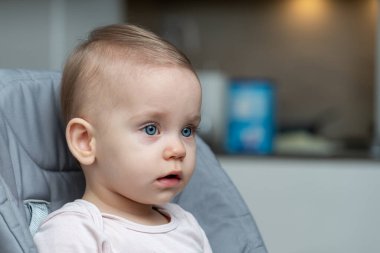 Mavi gözlü düşünceli bebek rahat bir mutfak ortamında oturuyor.